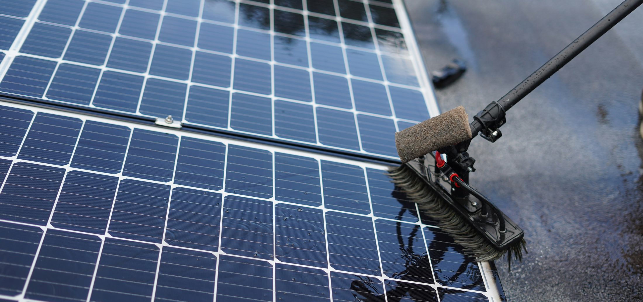 A technician cleaning a rooftop solar panel with a wet brush on a telescopic pole